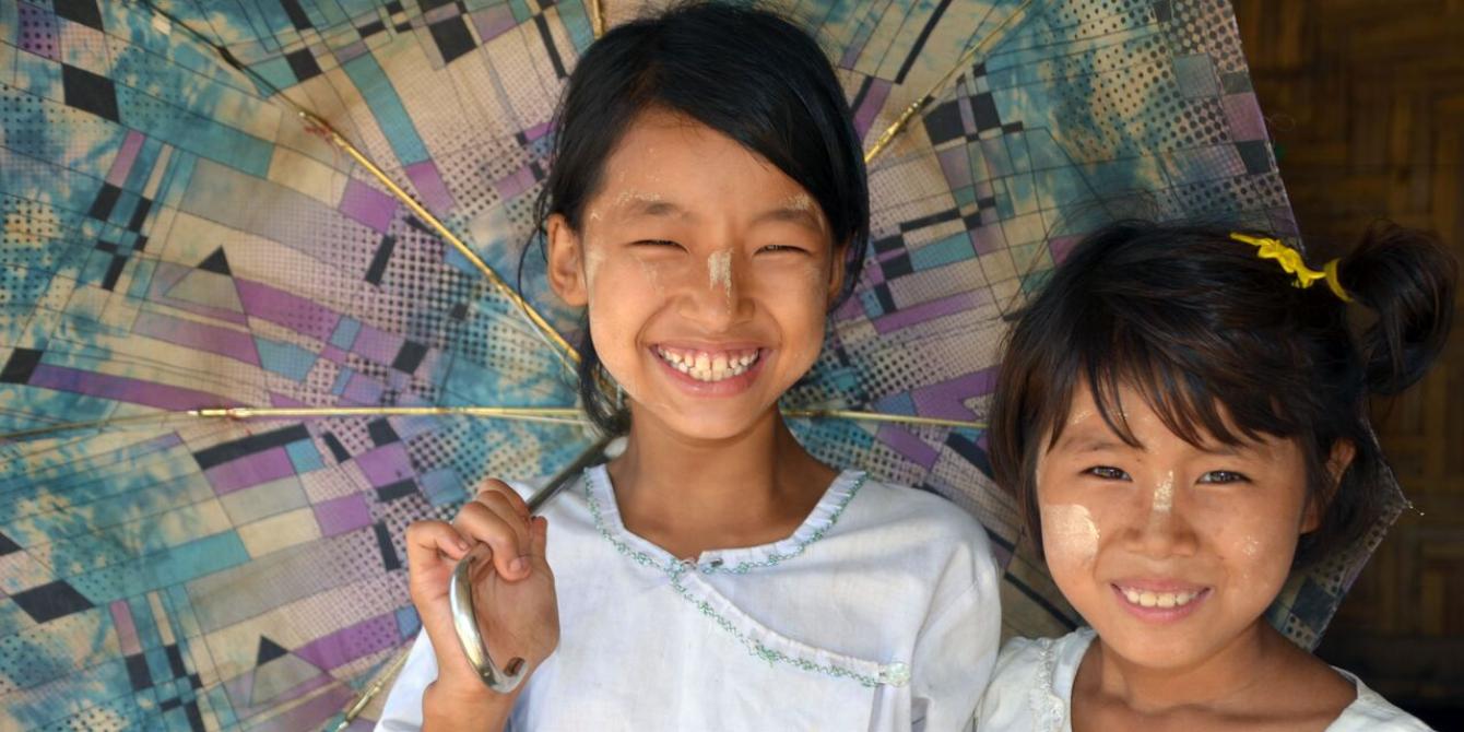 School Girls in Kachin IDPs camp, Photo by: Dustin Barter/ Oxfam Two shool girls are smiling under their umbrella, in Kachin IDPs camp. Photo by: Dustin Barter/ Oxfam